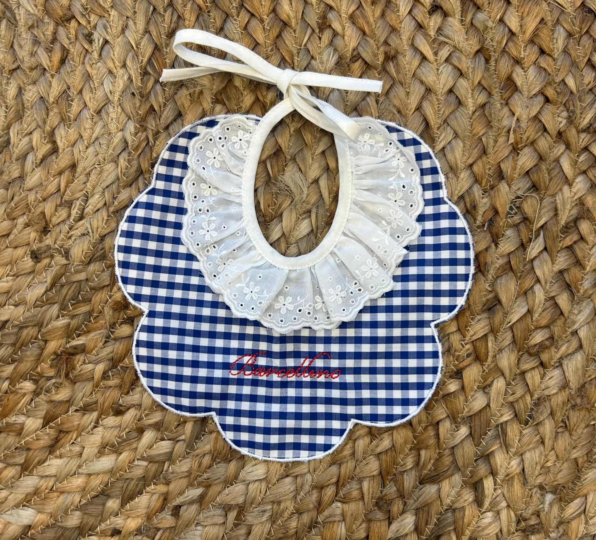 Bavaglino elegante in tessuto vichy blu e bianco con colletto in sangallo bianco e scritta ricamata Barcellino in rosso.