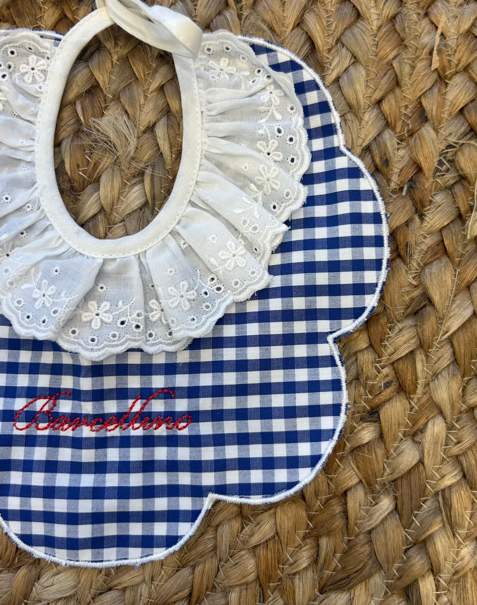 Bavaglino elegante in tessuto vichy blu e bianco con colletto in sangallo bianco e scritta ricamata Barcellino in rosso.