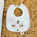 Uscita clinica neonata in ciniglia panna con ricamo floreale a cuore e fiocco rosa composta da tutina, bavetta, cappellino, lenzuola coordinate e copertina sfoderabile.