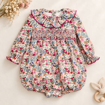 Pagliaccetto bimba floreale in cotone con punto smock e colletto a volant fucsia.