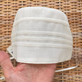 Cuffietta battesimale bianca unisex in cotone e lino con pieghe decorative frontali.