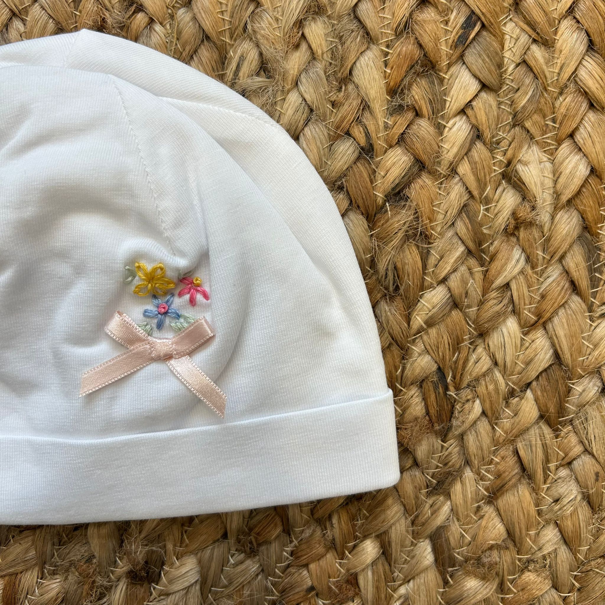 Cappellino neonato bianco con fiocchetto rosa e ricami floreali
