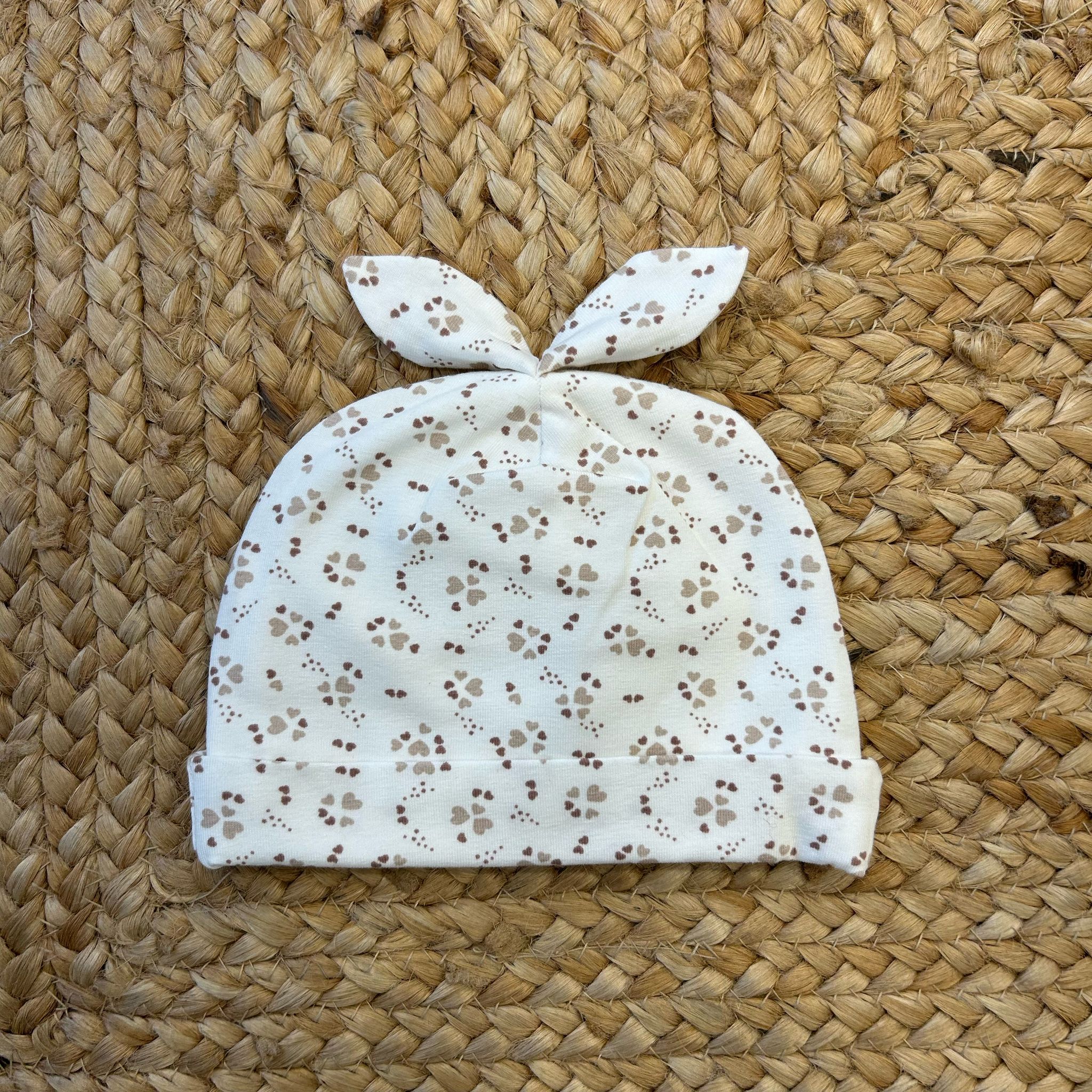 Cuffietta neonata in cotone con nodo e stampa a cuoricini beige.