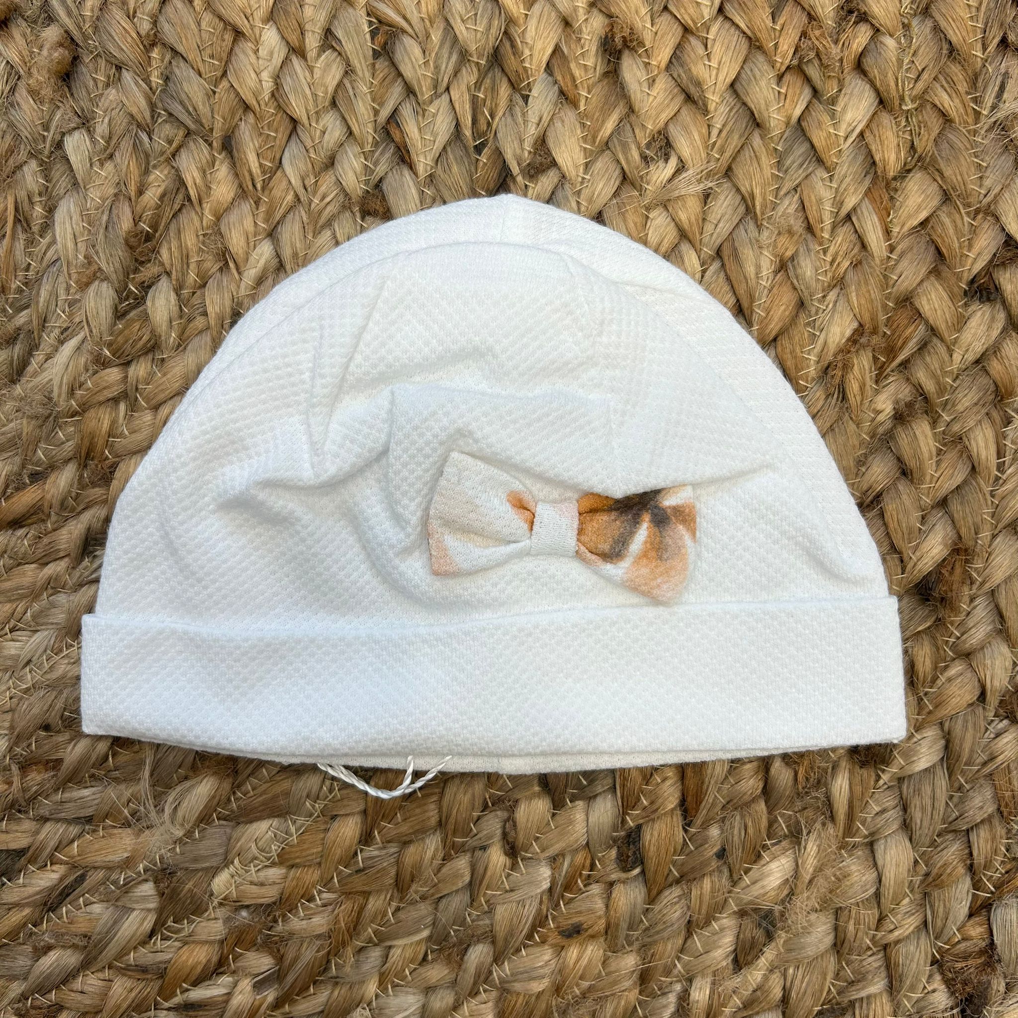 Cuffia neonata bianca con fiocco floreale nei toni pesca e beige.

