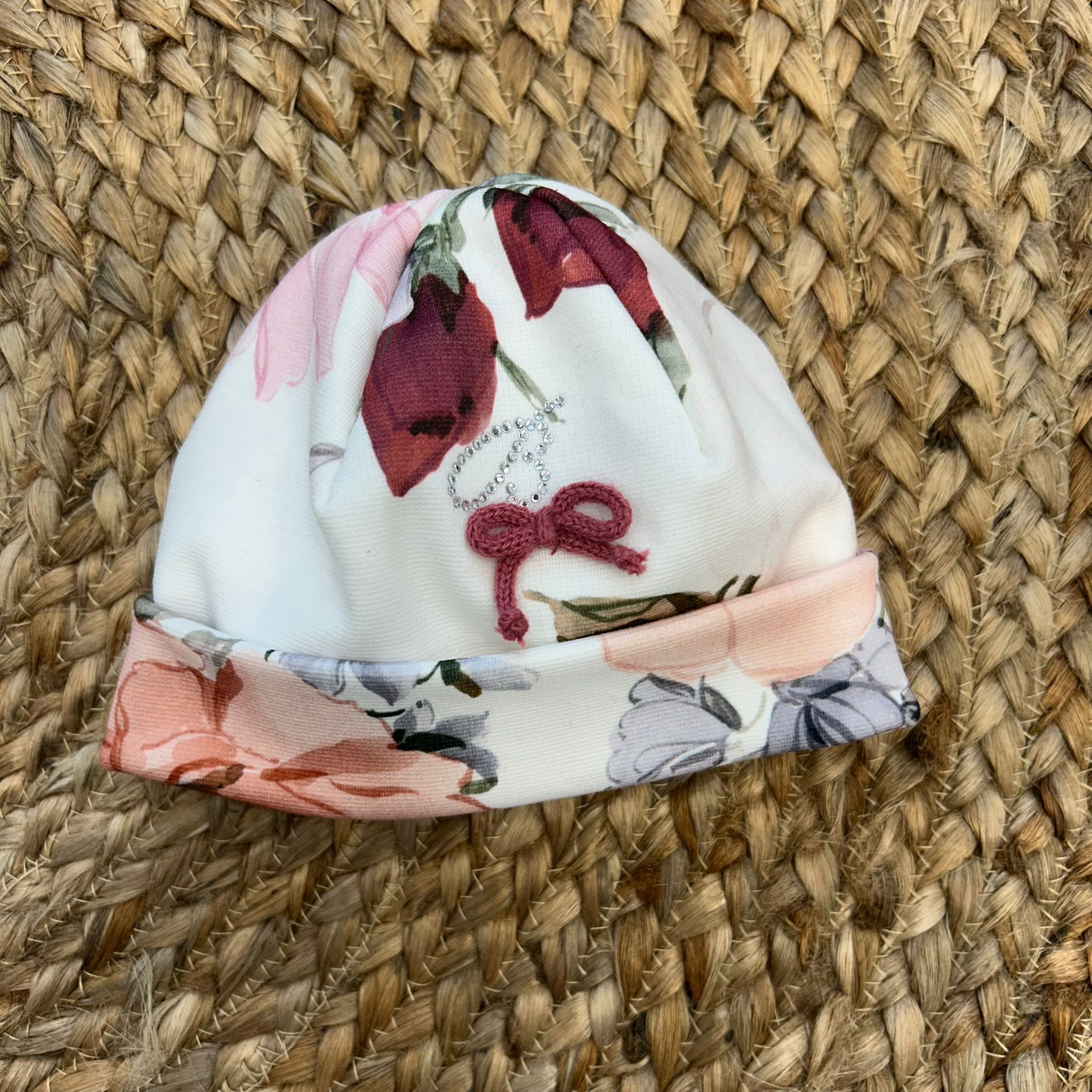 Cappellino neonata floreale con fiocco bordeaux e strass decorativi.