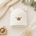 Cappellino neonata panna in caldo cotone con orsetto e fiocchetto rosa, ideale per corredino nascita, set nascita e primo cambio.