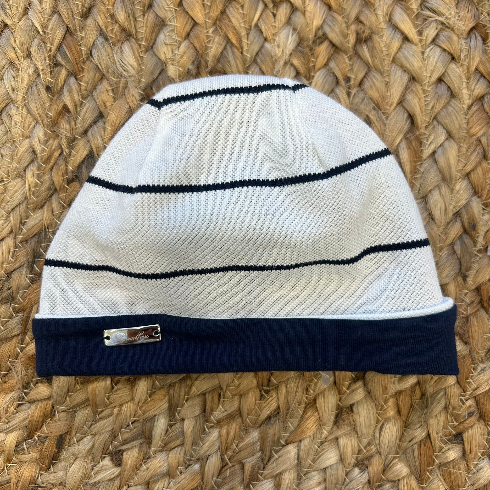 Cappellino neonato bianco con righe blu navy, bordo a costine blu e placchetta Barcellino.