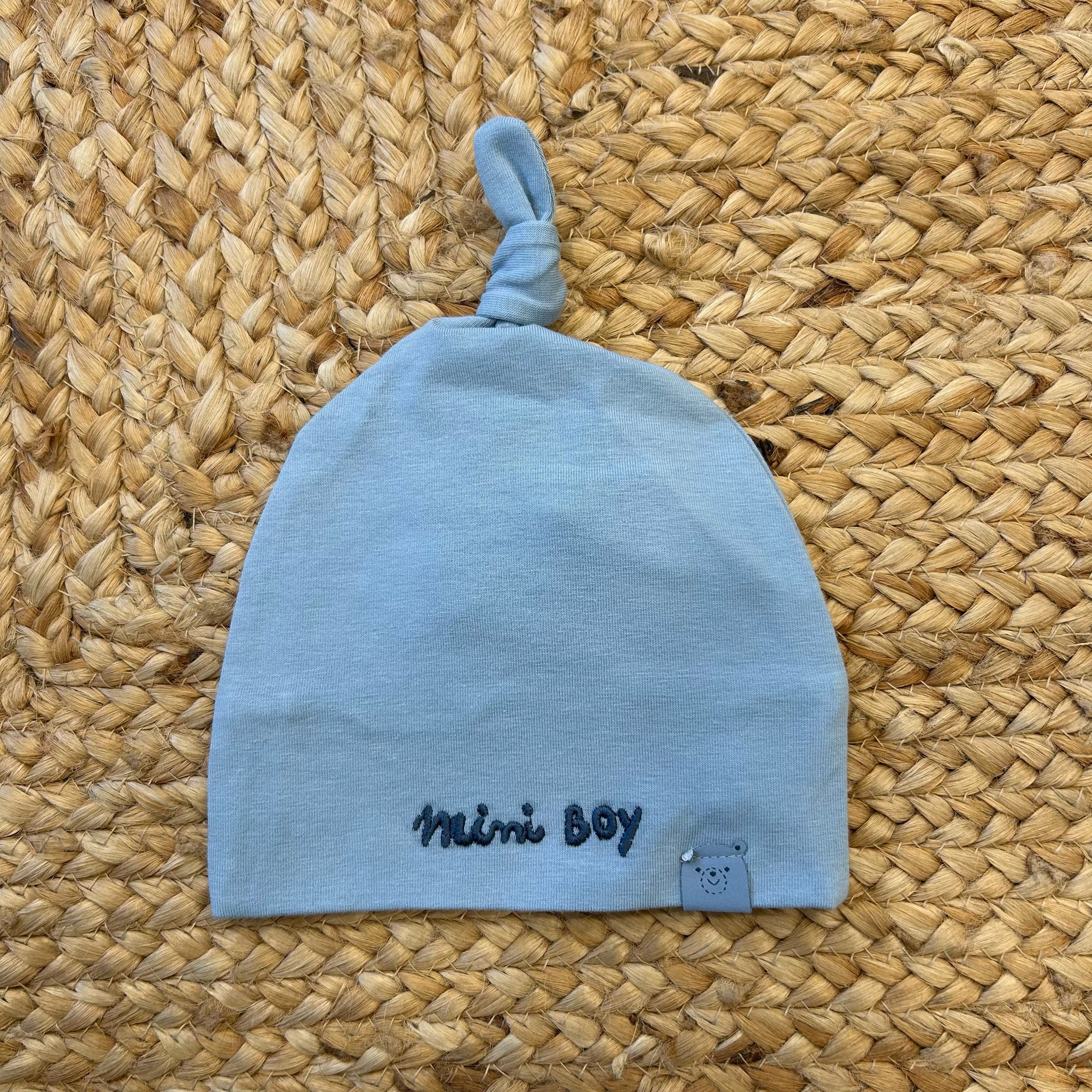 Cappellino neonato azzurro con nodo e scritta “Mini Boy” ricamata in blu.