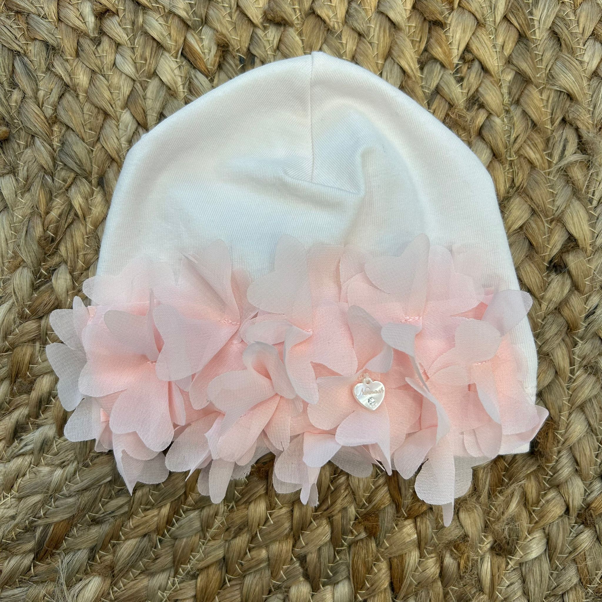 Cappellino neonata bianco con applicazione di petali rosa a forma di cuore in rilievo.

