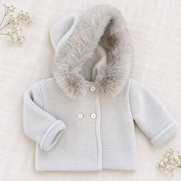 Cappottino battesimo bimbo beige chiaro in maglia con ampio cappuccio bordato effetto pelliccia, bottoni chiari e maniche lunghe.