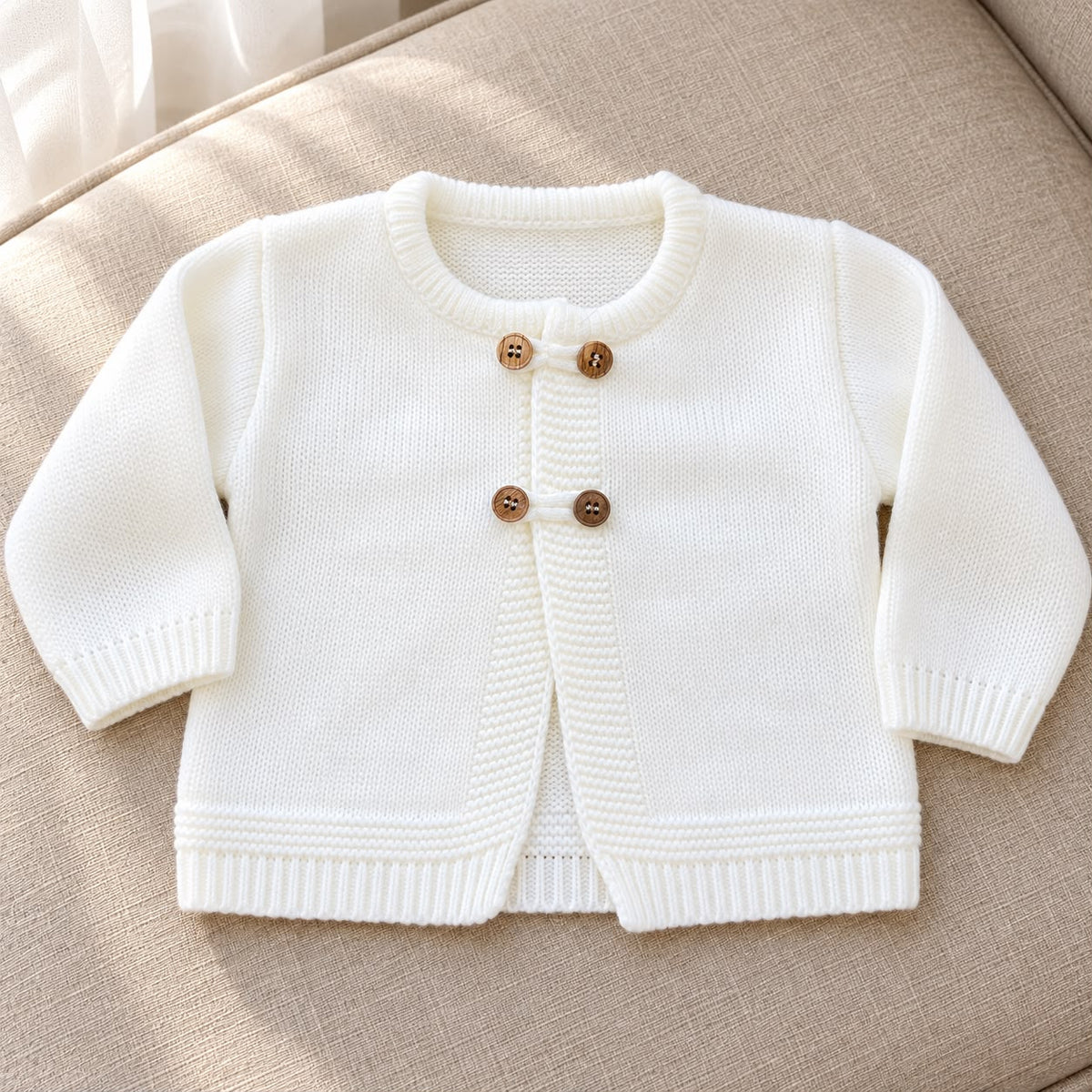Cardigan battesimo bimbo color panna in maglia 100% acrilico, con maniche lunghe, scollo rotondo e doppi bottoni effetto legno.