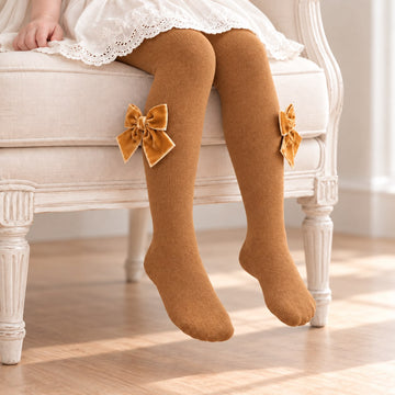 Collant bambina color caramello indossati, con grandi fiocchi laterali in velluto tono su tono sotto il ginocchio.