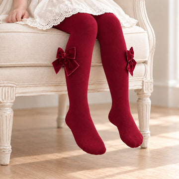 Collant bimba bordeaux indossati, con grandi fiocchi decorativi in velluto rosso vino applicati lateralmente su entrambe le gambe.