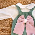 Dettaglio del fiocco rosa sulla salopette verde in maglia, con camicina bianca e colletto – corredino neonata elegante