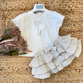 Completo bambina estivo in cotone avorio con gonna a balze in lino beige, fiocco decorativo e dettagli floreali.