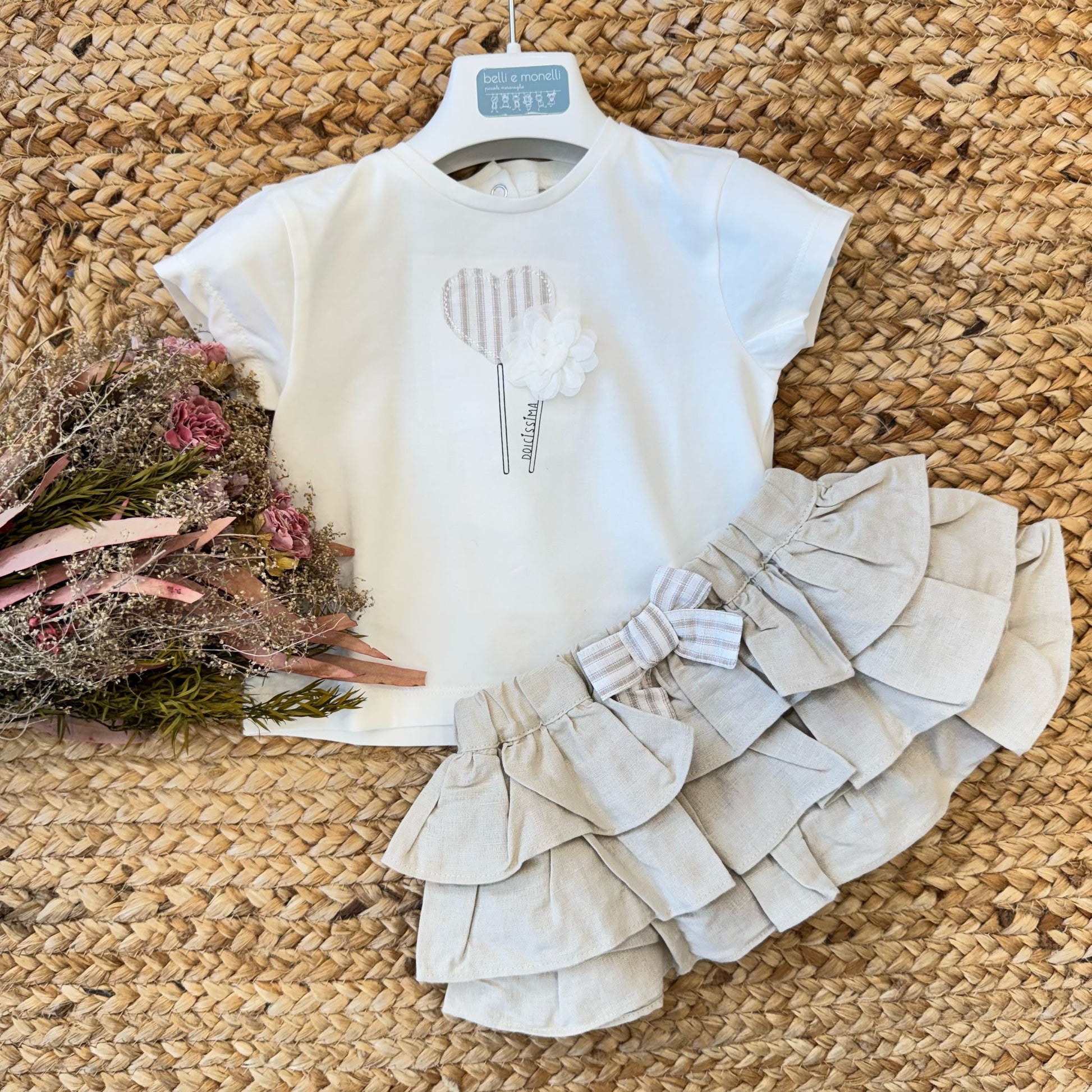 Completo bambina estivo in cotone avorio con gonna a balze in lino beige, fiocco decorativo e dettagli floreali.