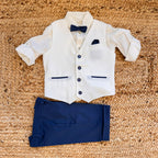 Completo elegante bambino con gilet panna, camicia, papillon blu e pantaloni blu navy per cerimonia.

