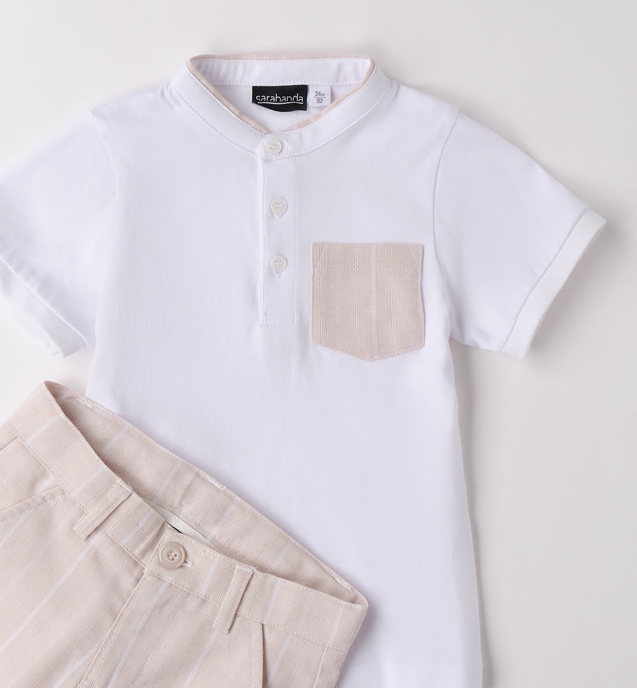 Completo bambino con t-shirt bianca con colletto e taschino e pantaloncini beige a righe verticali.