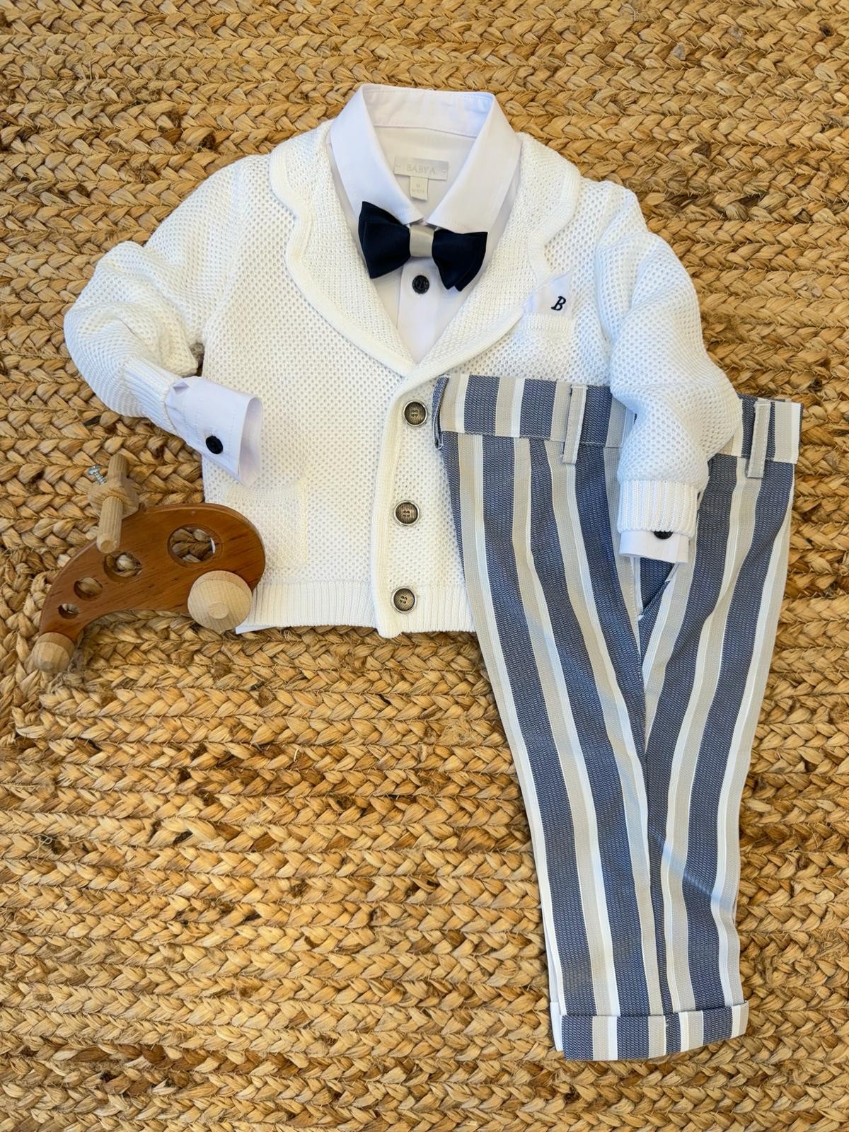 Completo battesimo bimbo con cardigan bianco in maglia, pantaloni a righe blu e beige e papillon coordinato, perfetto per cerimonie.