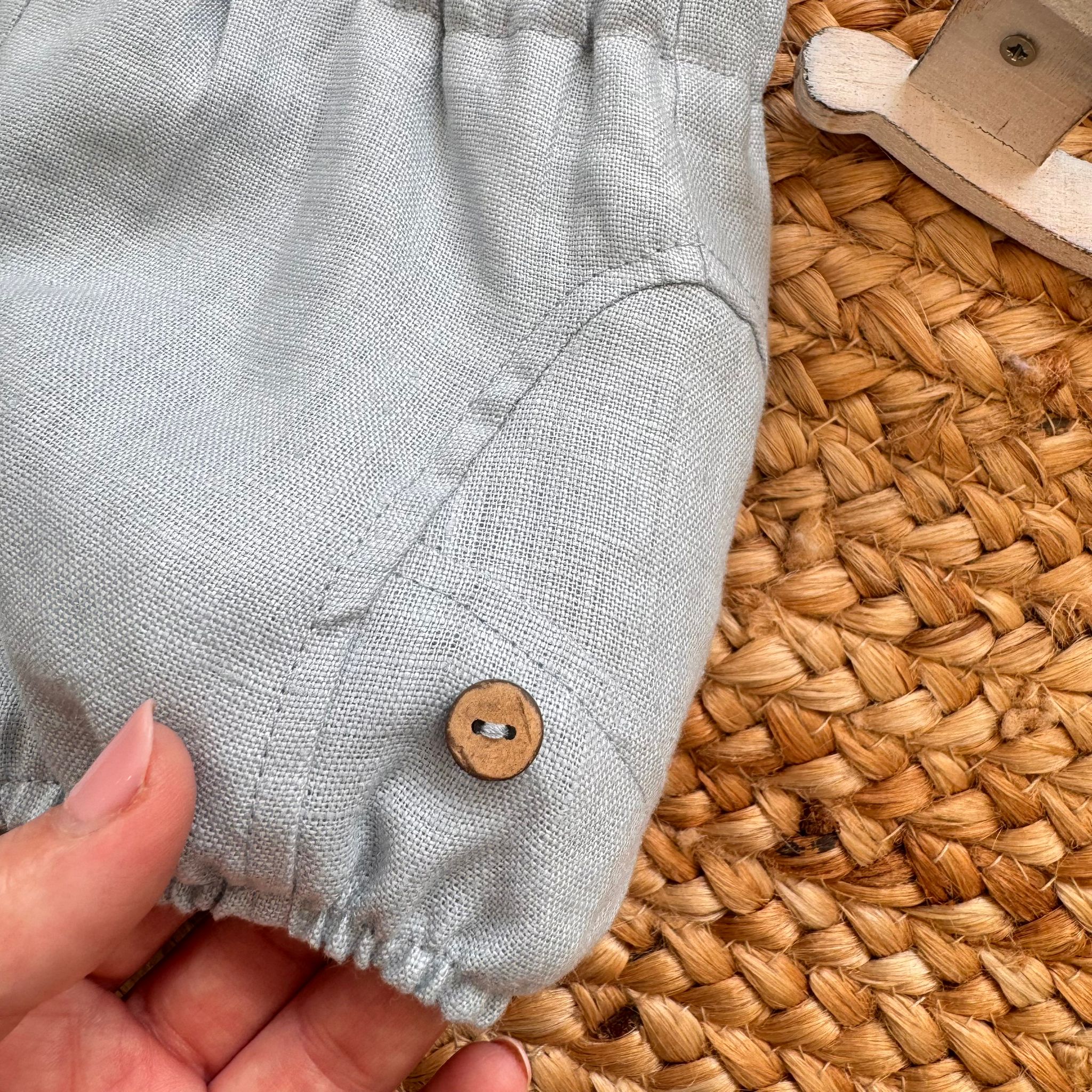 Dettaglio bottoncino in legno su pantaloncino lino celeste