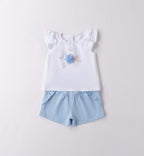 Dettaglio maglietta bianca con applicazione floreale e pantaloncini azzurri.