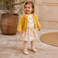 Bimba con cardigan giallo, maglia bianca e gonna con piccoli fiori gialli