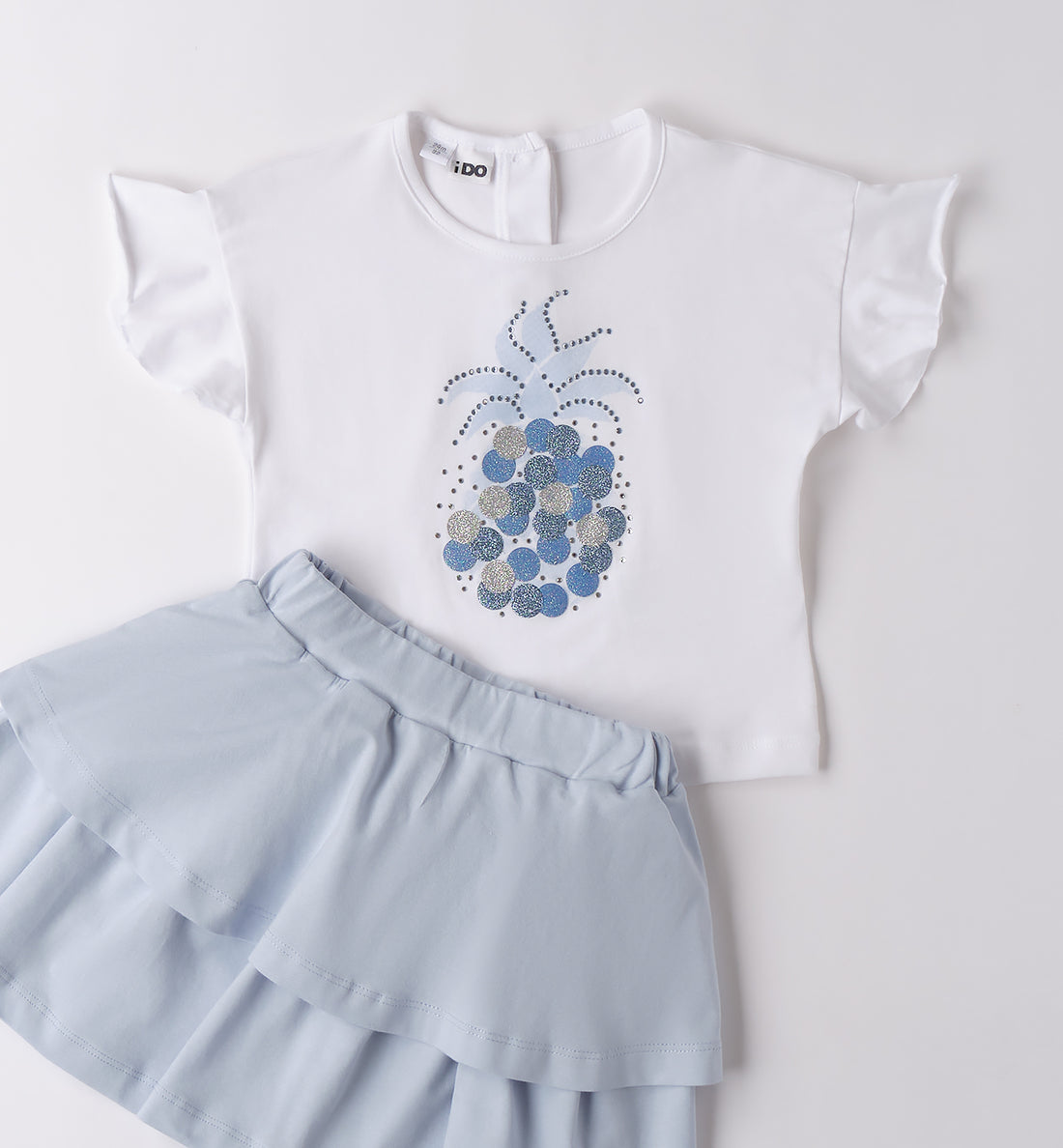Completo bambina con t-shirt bianca ananas glitter e gonna azzurra a balze.