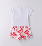 Outfit bambina estivo con t-shirt bianca a cuore floreale e pantaloncini a fiori rossi e blu, ideale per cerimonie informali e eventi primaverili.