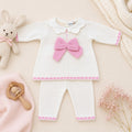 Dettaglio tutina neonata in misto lana bianca e rosa con maxi fiocco in maglia, colletto e lavorazione traforata.