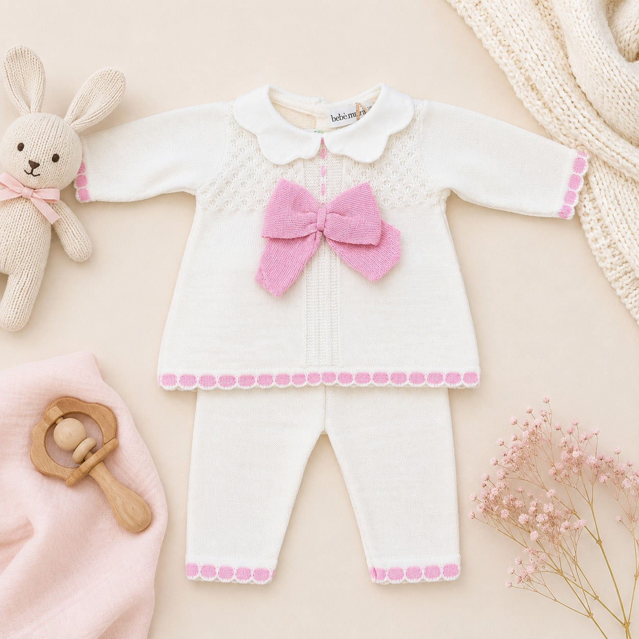 Dettaglio tutina neonata in misto lana bianca e rosa con maxi fiocco in maglia, colletto e lavorazione traforata.