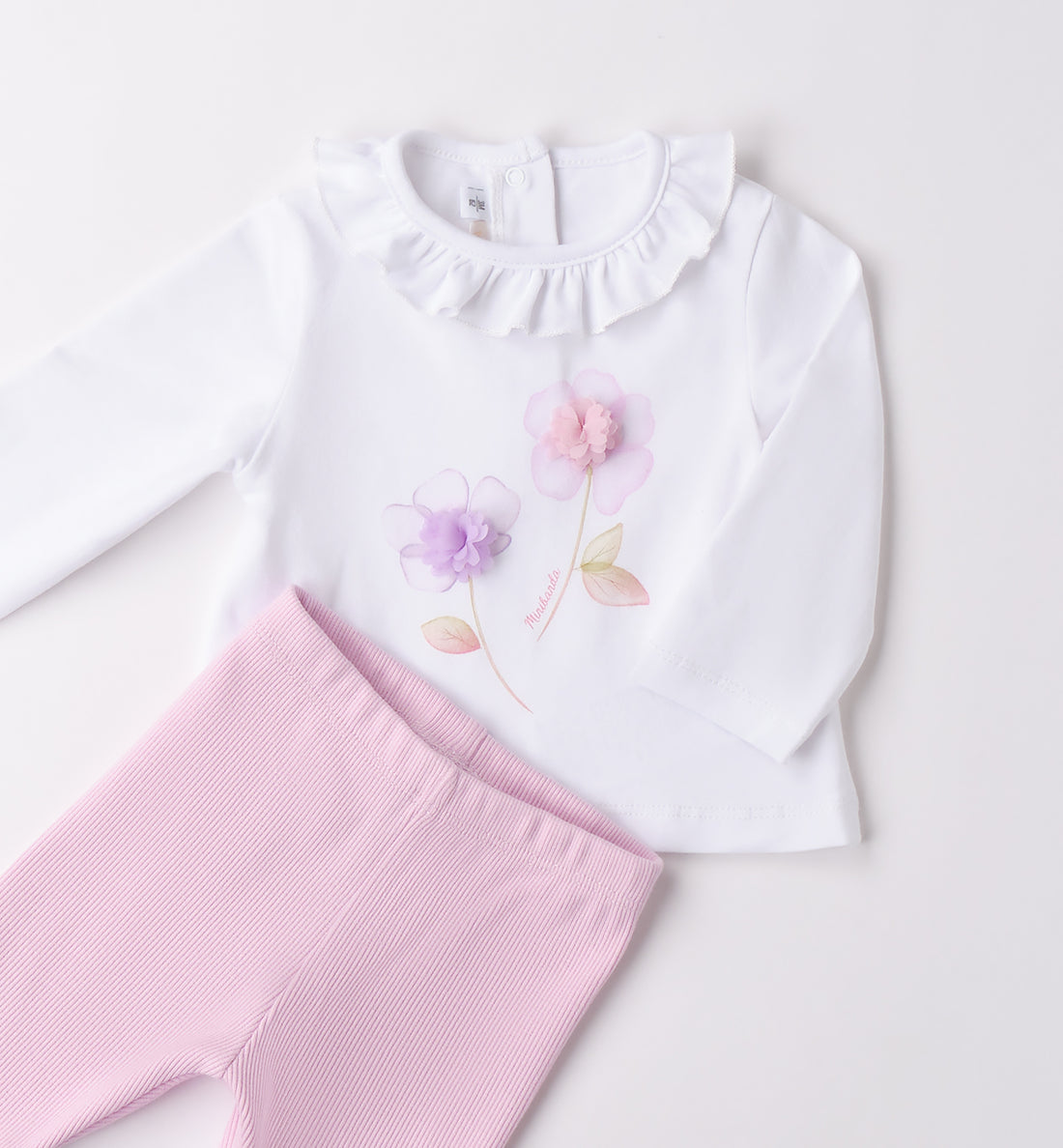 Completo neonata con blusa bianca a volant e leggings rosa, vista frontale.