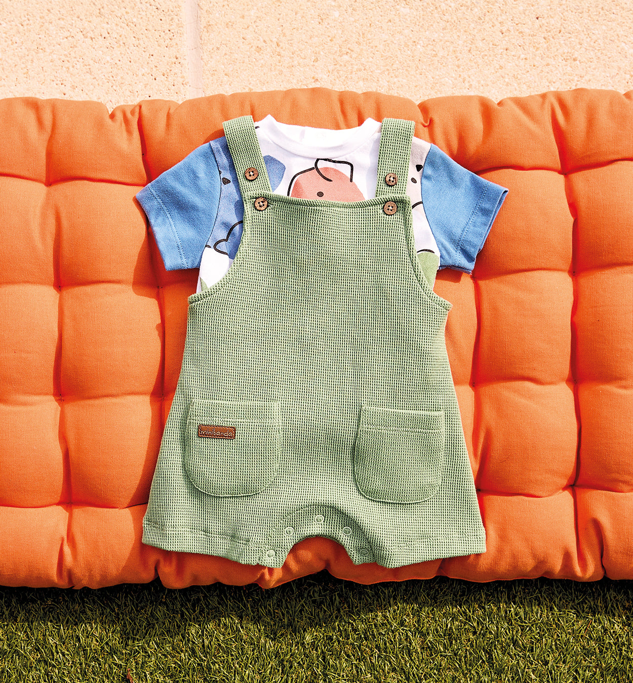 Completo neonato con salopette verde in maglina e t-shirt con maniche blu e stampa astratta.