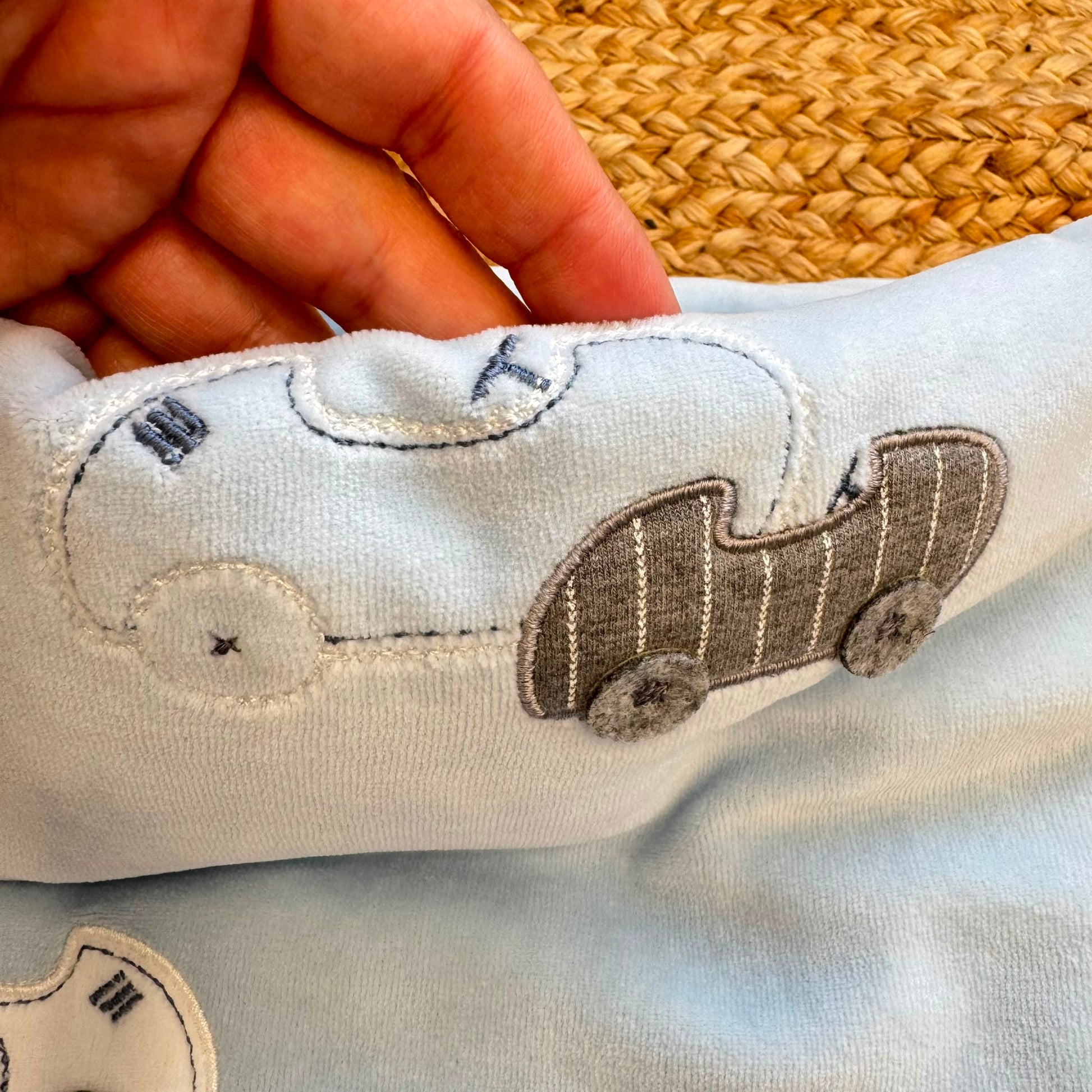 Dettaglio applicazioni macchinine bianche e grigie sulla copertina neonato in ciniglia azzurra.