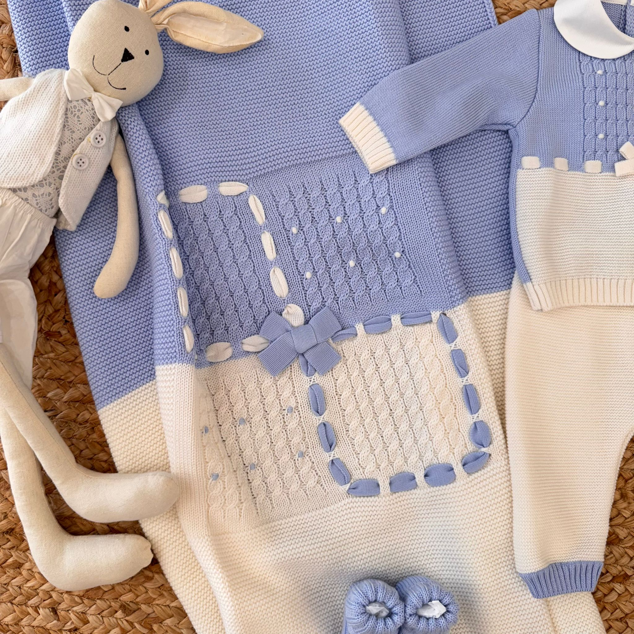 Copertina in lana merino lavorata a maglia con quadri ricamati azzurri e panna e fiocco centrale