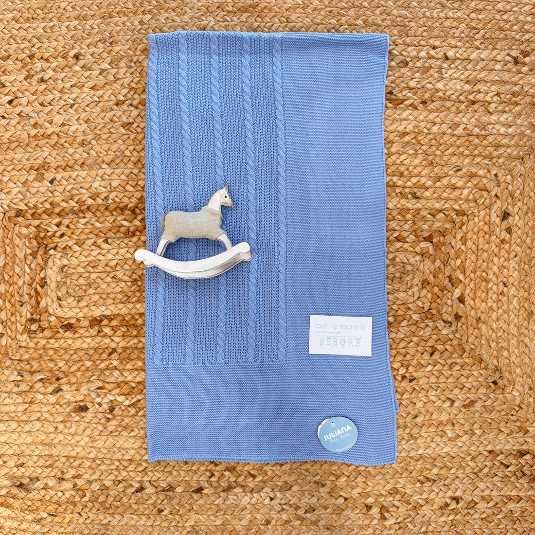 Copertina in maglia azzurra per neonato con lavorazione a treccia e cavallino in legno