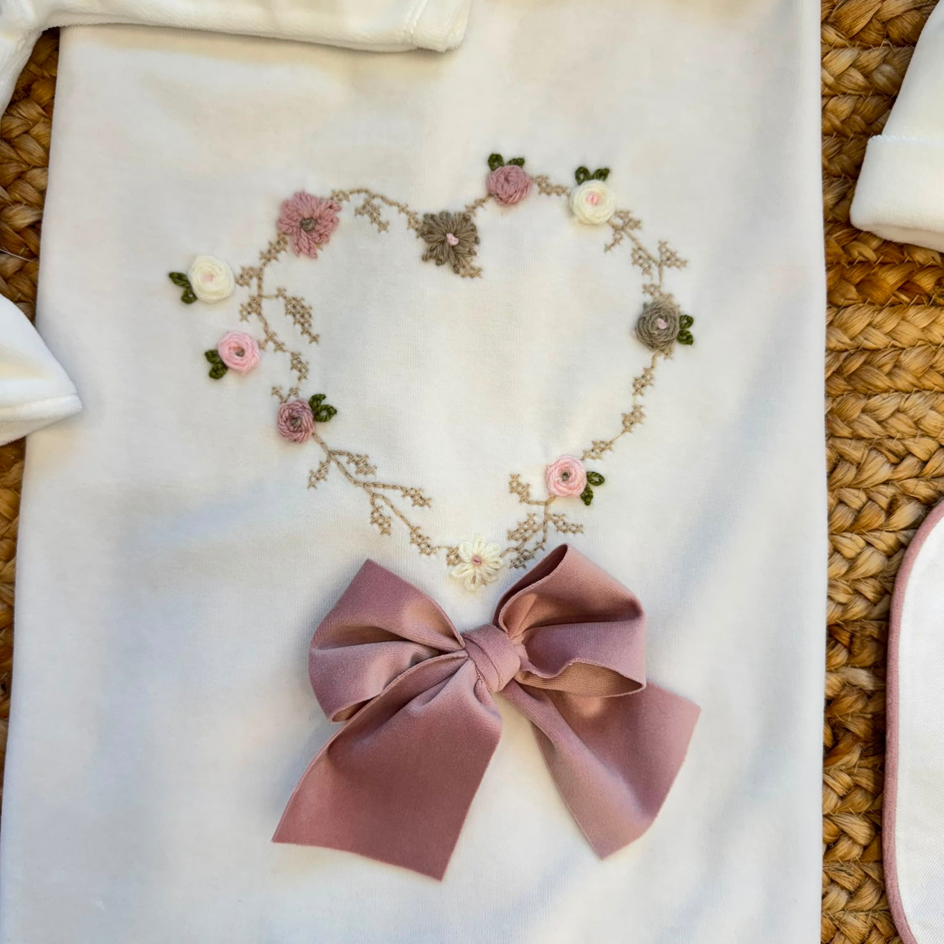 Uscita clinica neonata in ciniglia bianca e rosa con completino ricamato a cuore floreale, fiocco applicato, cappello, bavetta, scarpine, lenzuola coordinate e copertina sfoderabile.