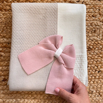  Copertina in maglia rosa e panna per neonata piegata, con maxi fiocco centrale in tinta