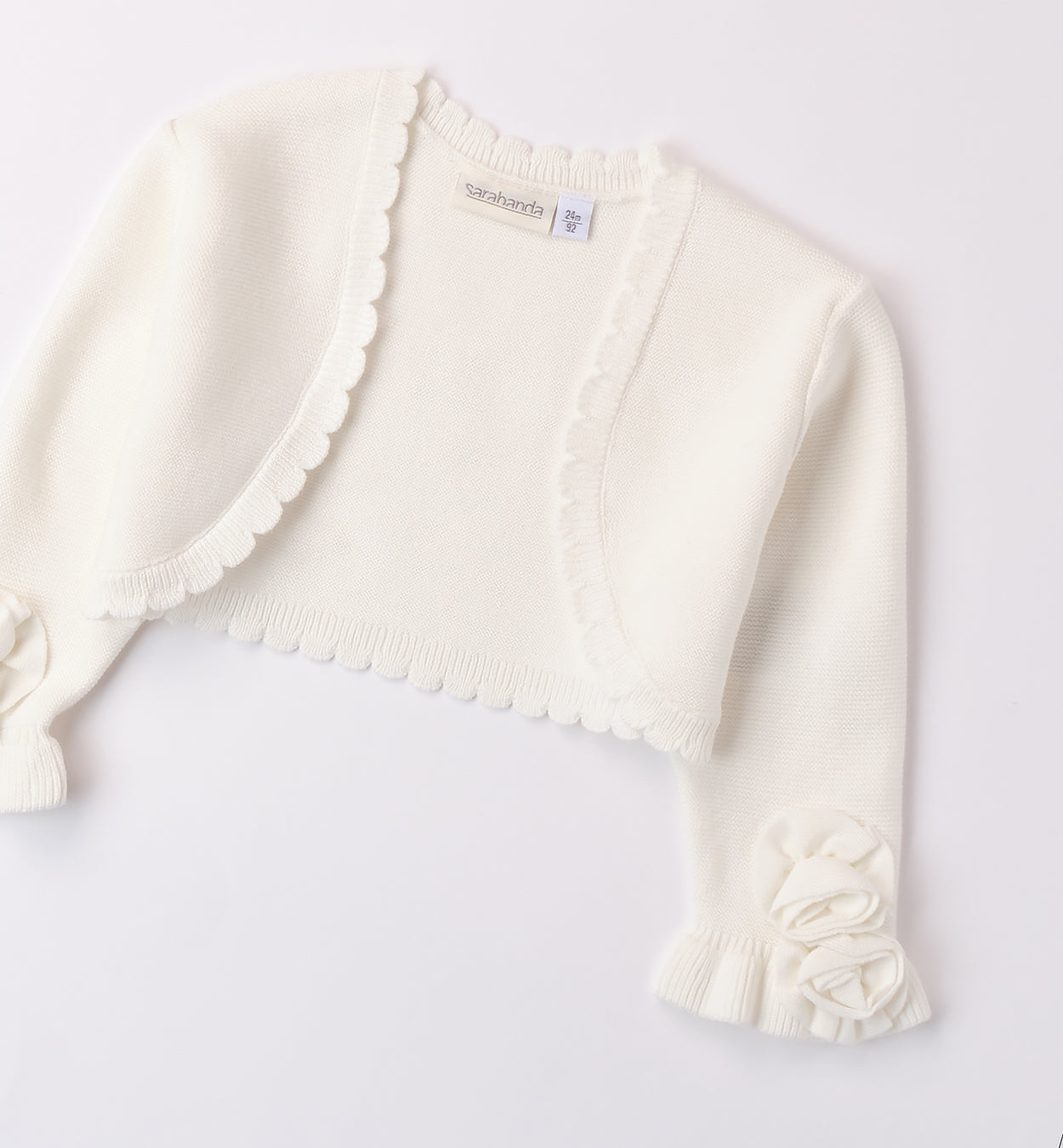 Coprispalle in maglia bianca per bambina con fiori decorativi sulle maniche.

