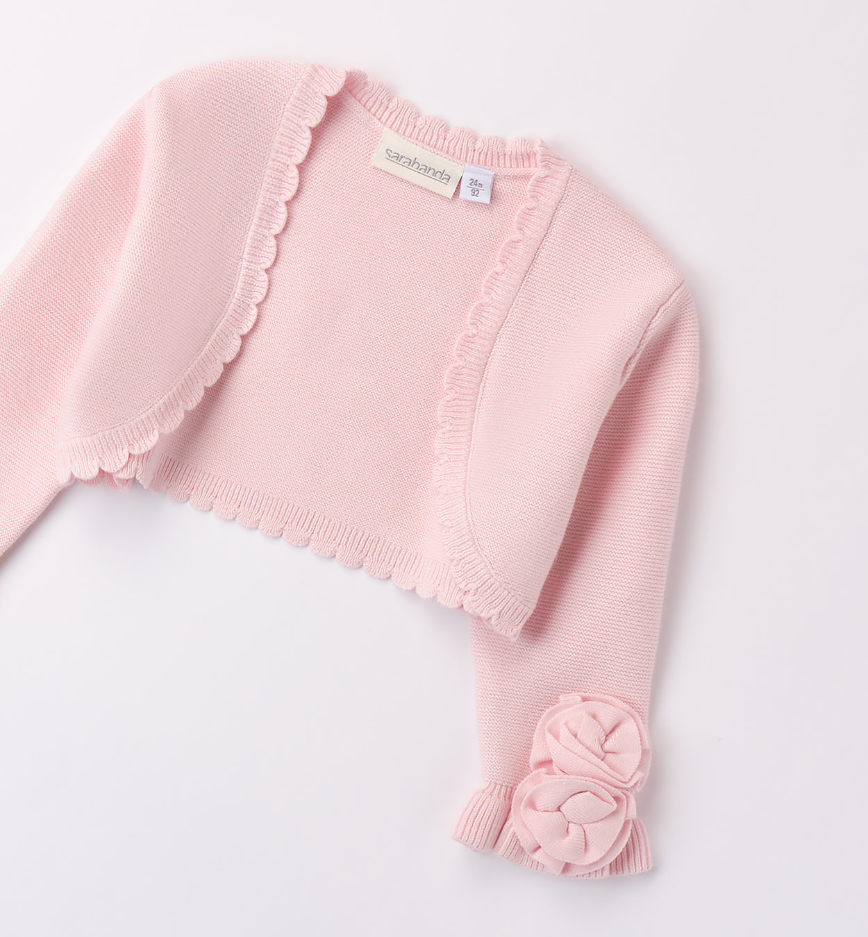 Coprispalle rosa cipria in maglia per bambina con dettagli floreali e bordo smerlato.