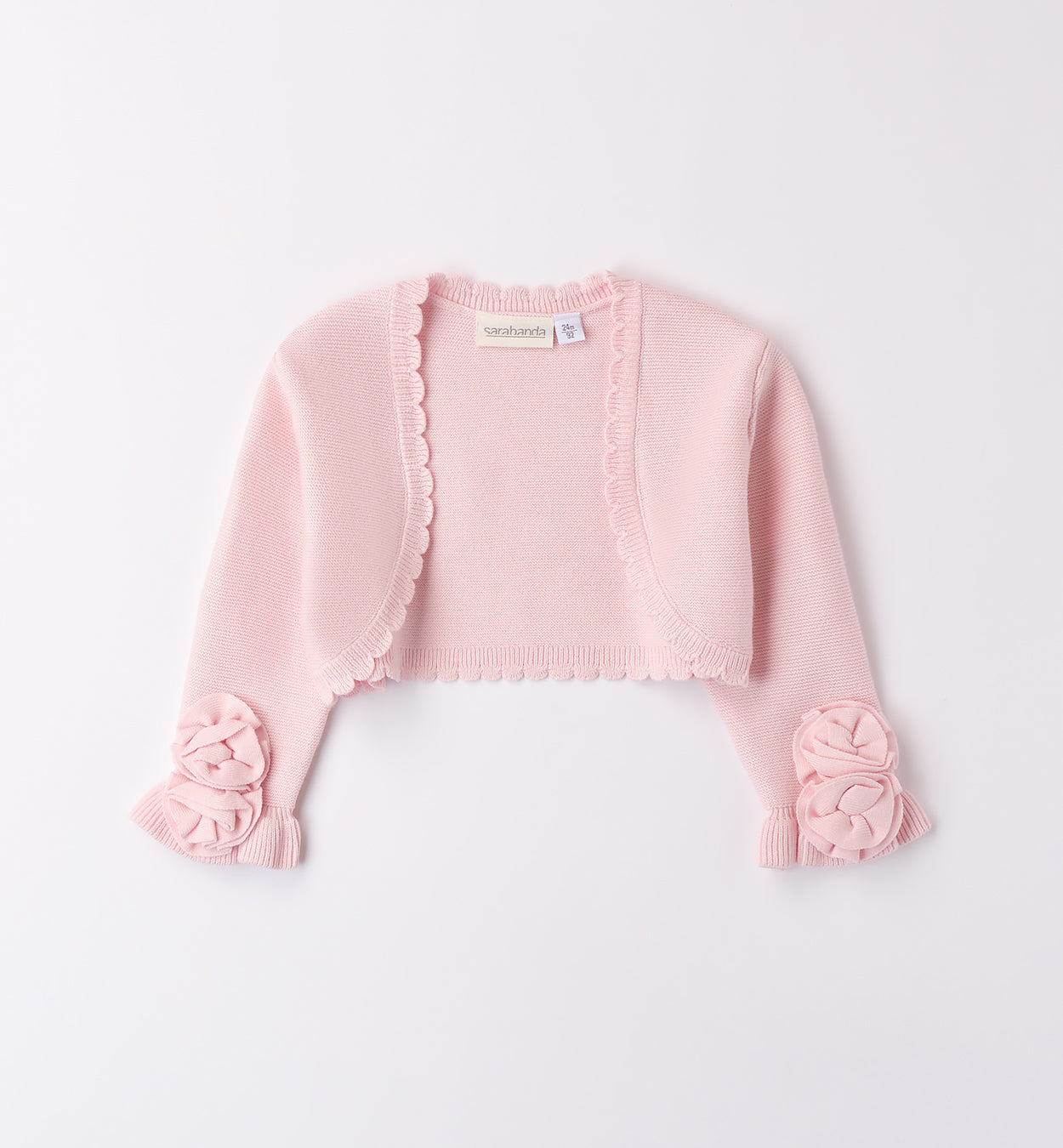 Coprispalle rosa cipria in maglia per bambina con dettagli floreali e bordo smerlato.
