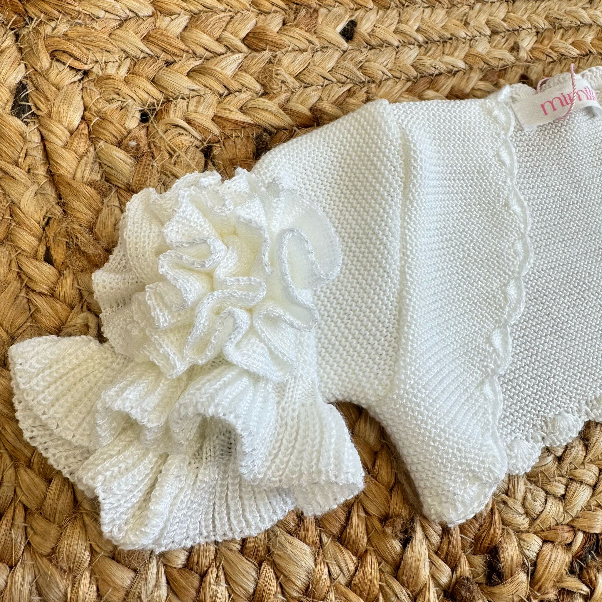 Dettaglio maniche con balze e fiore applicato sul coprispalle in maglia avorio per bambina.
