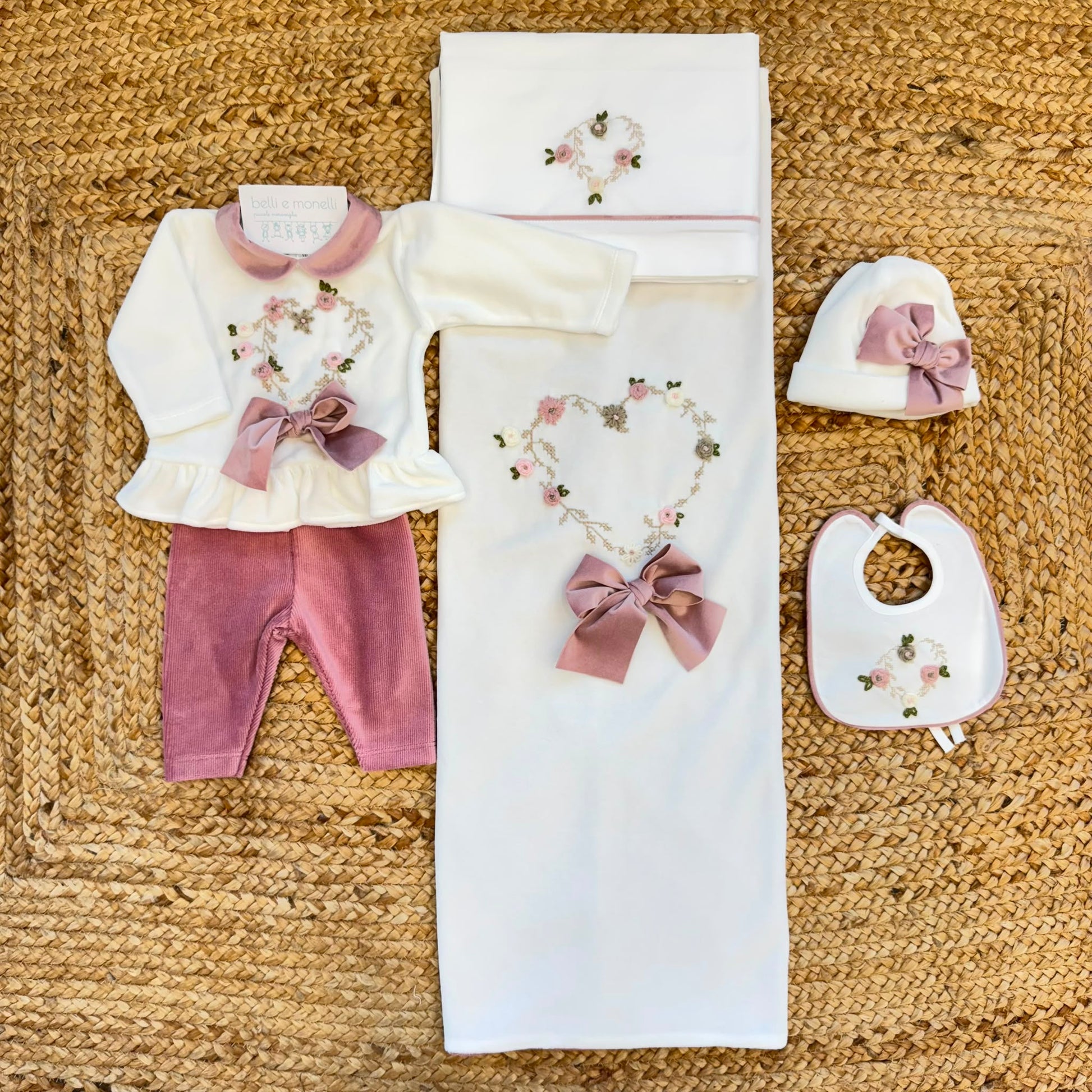 Uscita clinica neonata in ciniglia bianca e rosa con completino ricamato a cuore floreale, fiocco applicato, cappello, bavetta, scarpine, lenzuola coordinate e copertina sfoderabile.