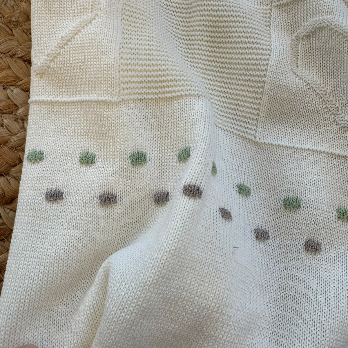 Dettaglio maglia del corredino neonata con piccoli pois verde salvia e tortora