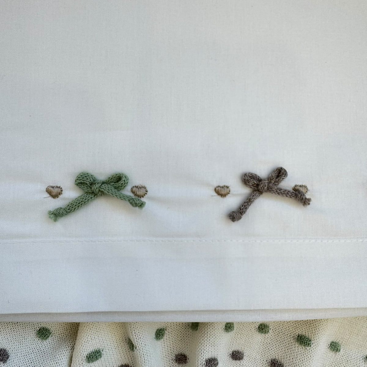 Dettaglio ricamo con fiocchetti sul lenzuolino del set nascita neonata