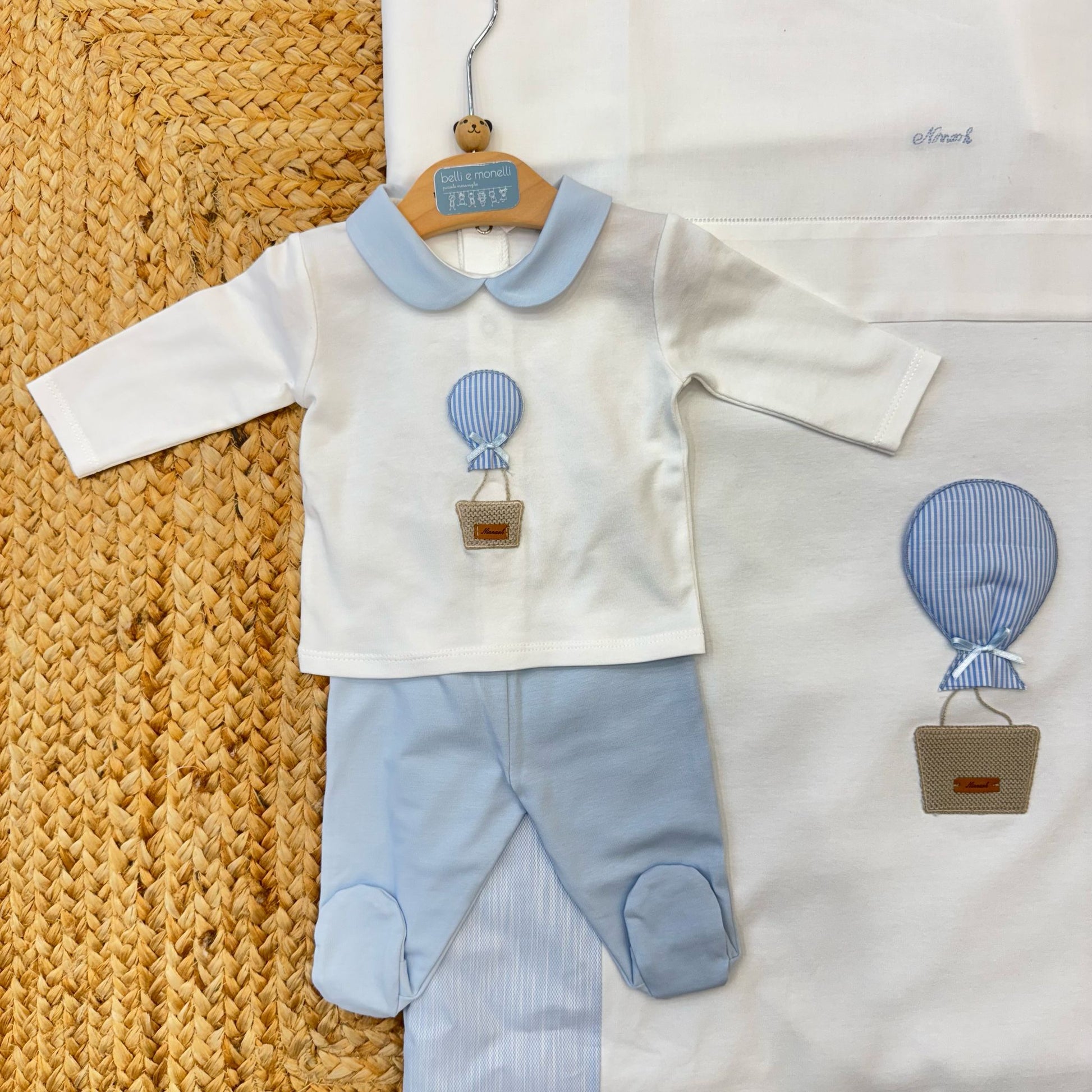 Set nascita neonato in cotone con tutina, cappellino e lenzuolino, decorato con un’applicazione mongolfiera in tessuto a righe azzurre. Perfetto per l’uscita dalla clinica e il primo corredino.