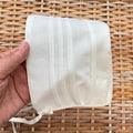 Cuffietta battesimale bianca unisex in cotone e lino con pieghe decorative frontali.