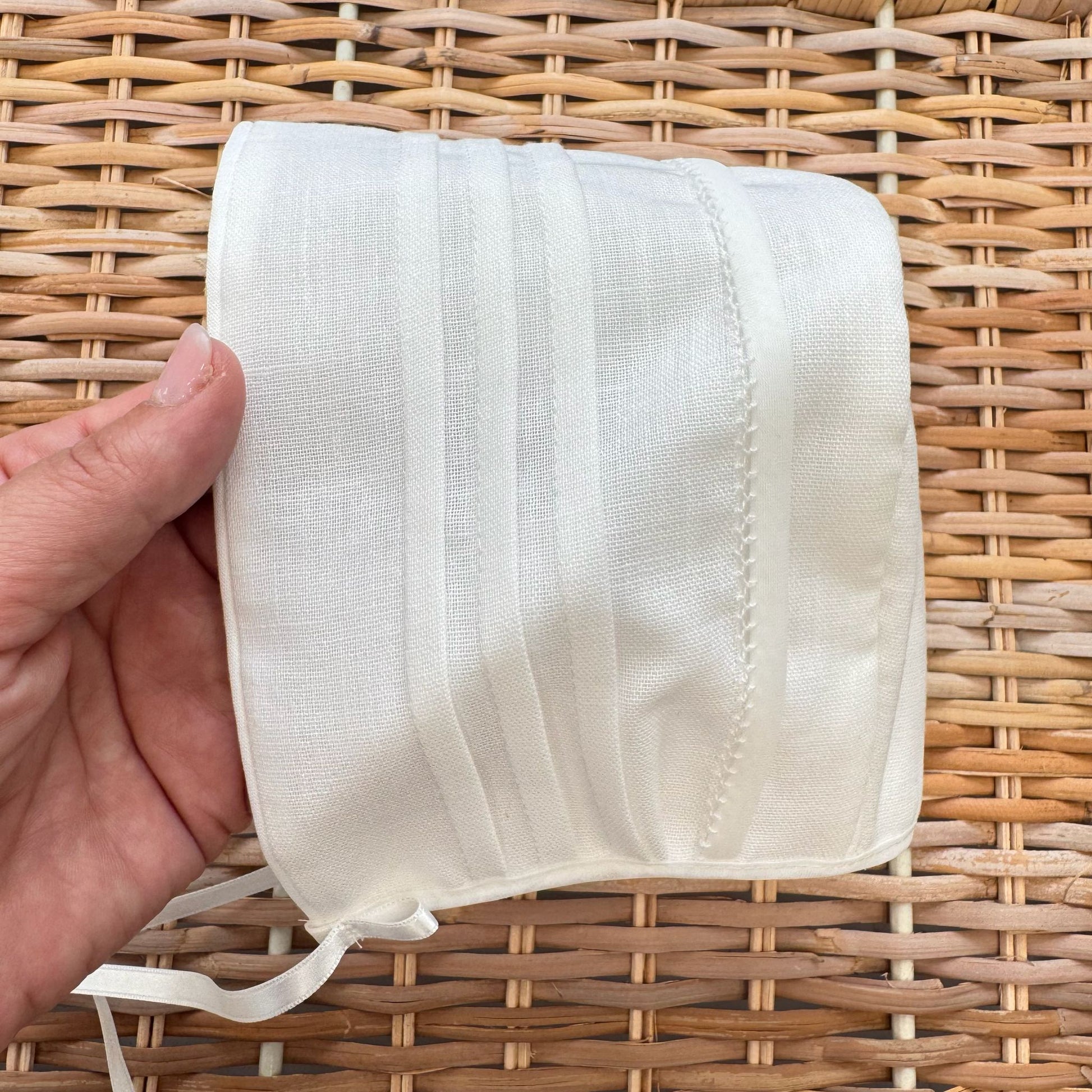 Cuffietta battesimale bianca unisex in cotone e lino con pieghe decorative frontali.