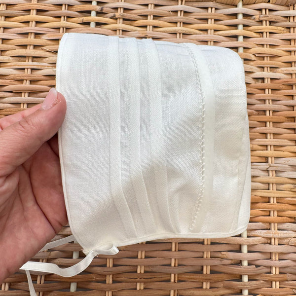 Cuffietta battesimale bianca unisex in cotone e lino con pieghe decorative frontali.