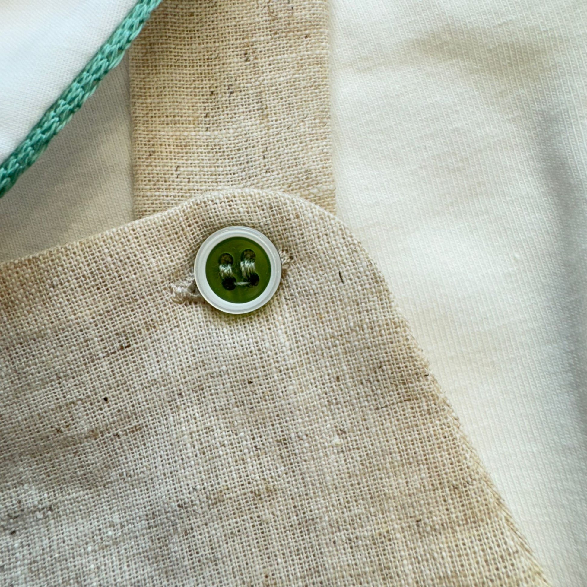 Dettaglio bottone verde su salopette in lino