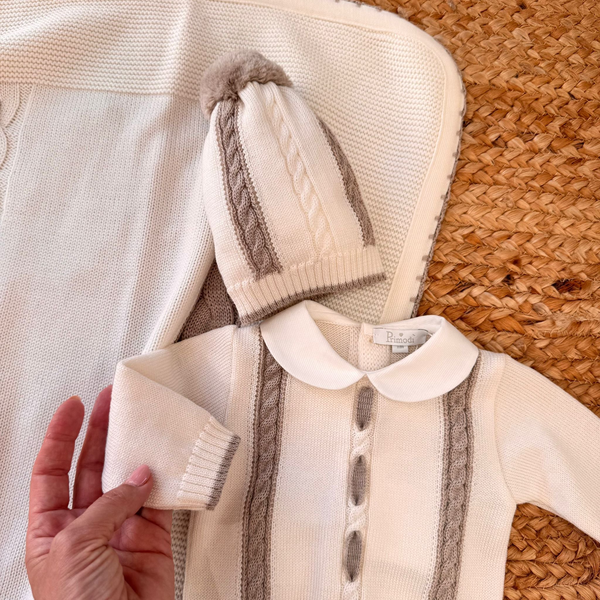 Primo piano su cappellino neonato e parte del completino in maglia con copertina coordinata panna e beige